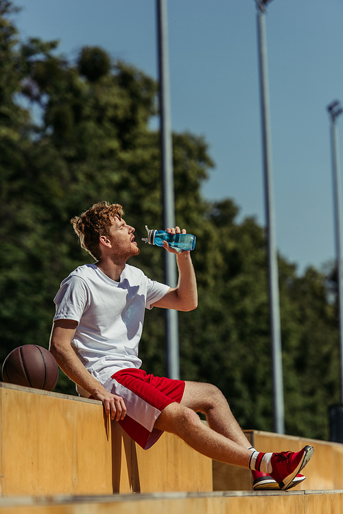 thirsty sportsman sitting on stadium and drinking fresh water from sports bottle