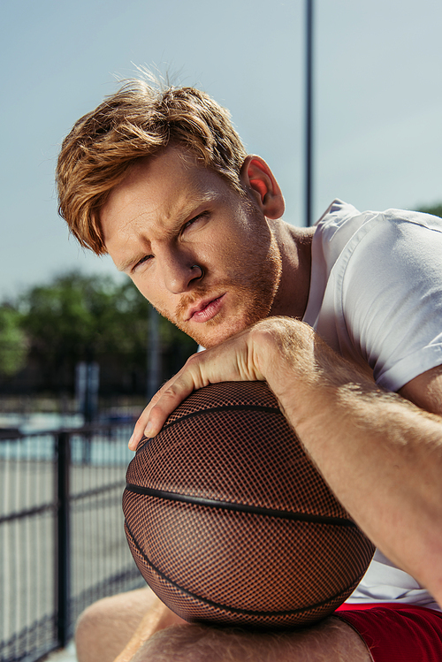 redhead basketball player looking at camera near ball outdoors