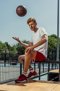 young man in sportswear sitting on bench and playing with ball