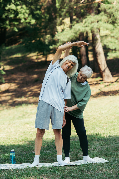 senior woman training happy husband with grey hair standing on fitness mat in park