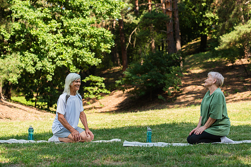 full length of happy senior couple in sportswear sitting on fitness mats in green park