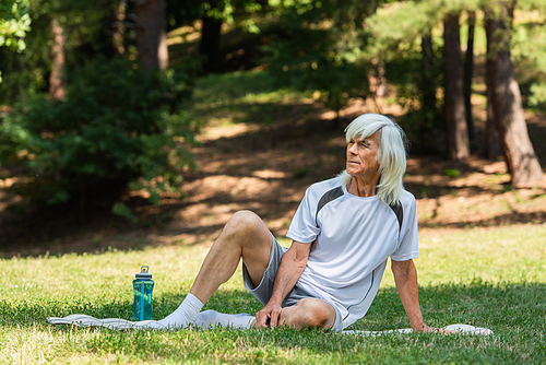 full length of retired man in sportswear sitting on fitness mat in green park