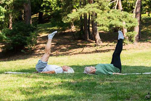 full length of senior couple in sportswear doing shoulder stand on fitness mats in green park