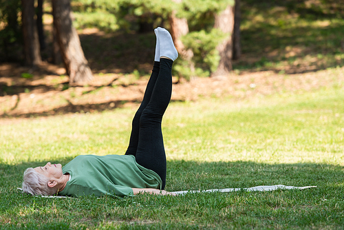 full length of senior woman with grey hair doing shoulder stand on fitness mat in park