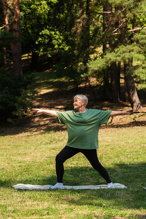 full length of senior woman with grey hair smiling and working out on fitness mat in park