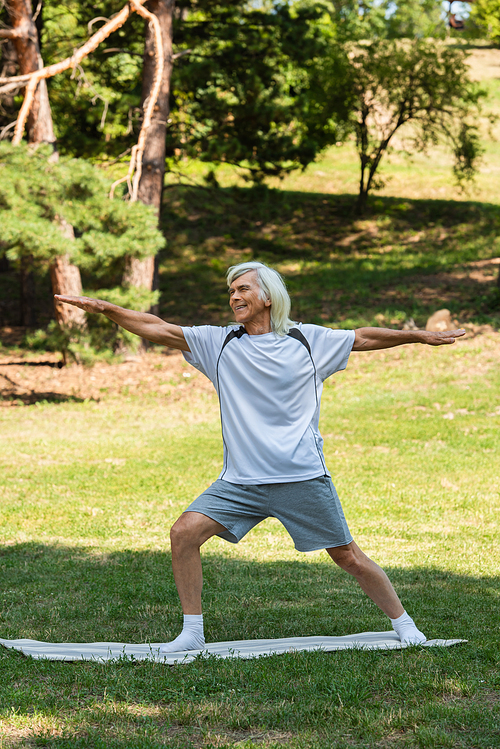 full length of cheerful senior man with grey hair smiling and working out with outstretched hands in park