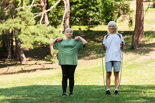full length of cheerful senior couple in sportswear exercising with sports equipment in green park