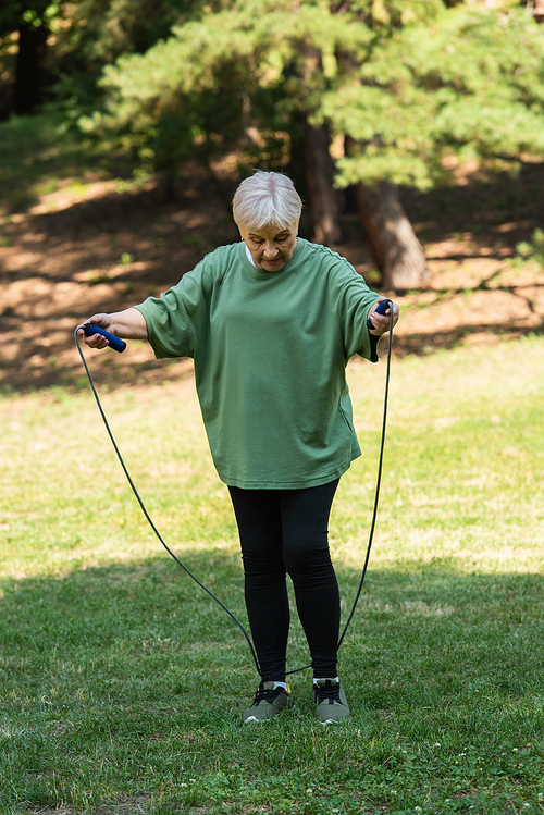 full length of senior woman with grey hair holding skipping rope in park