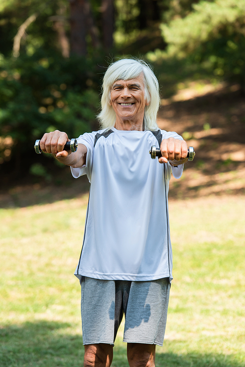 happy senior man in sportswear exercising with dumbbells in green park