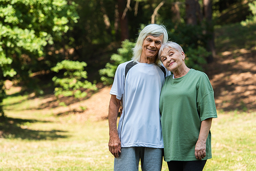 cheerful senior couple in sportswear hugging in green park