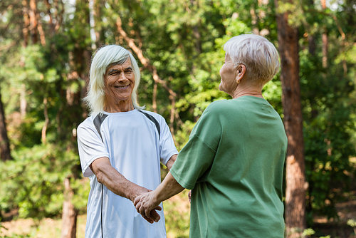 joyful senior couple in sportswear holding hands in green park