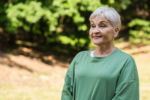happy and retied woman with grey hair standing in green t-shirt in park