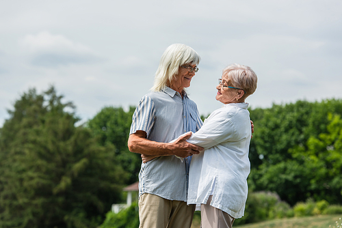 happy senior husband and wife with grey hair hugging in summer