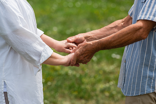 cropped view of senior husband and wife holding hands in summer