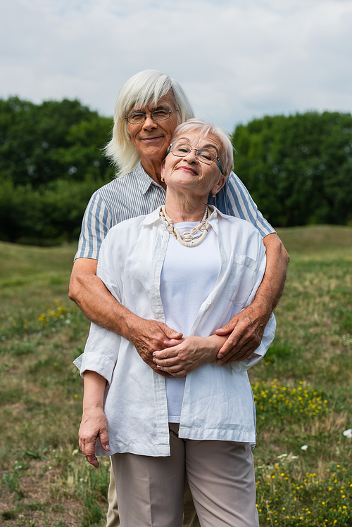 happy senior husband hugging wife with grey hair and standing in park