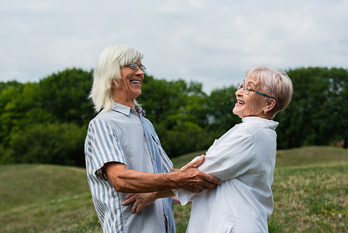 happy senior couple with grey hair looking at each other and smiling outside