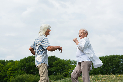 happy retired couple in glasses dancing and smiling outside