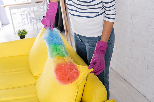 Cropped view of woman in rubber gloves cleaning couch with dust brush