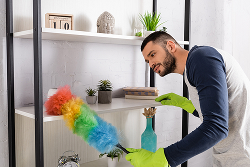 Young man in rubber gloves cleaning cupboard with dust brush