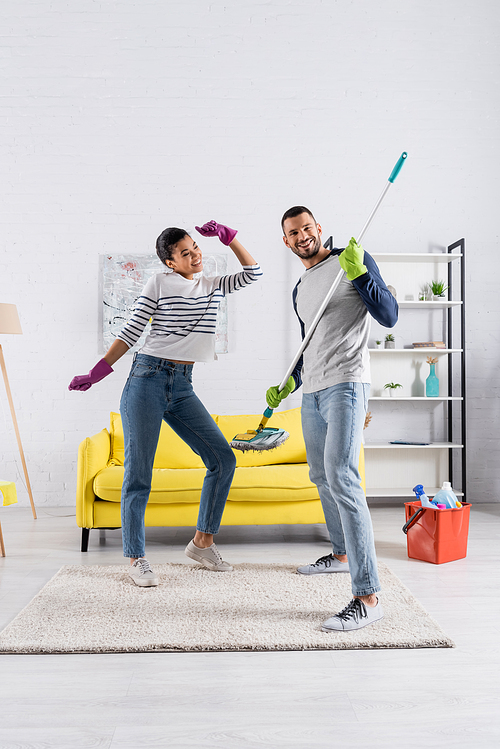 Smiling interracial couple with mop having fun in living room