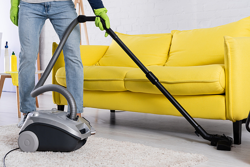Cropped view of man vacuuming floor near couch