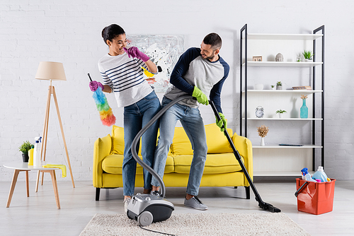 Positive interracial couple having fun while cleaning home
