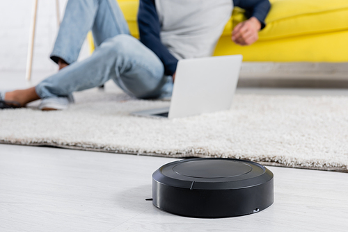Cropped view of robotic vacuum cleaner on floor near man using laptop at home