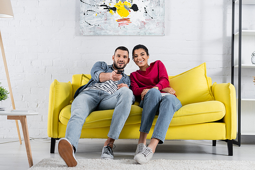 Young multiethnic couple watching film on couch at home