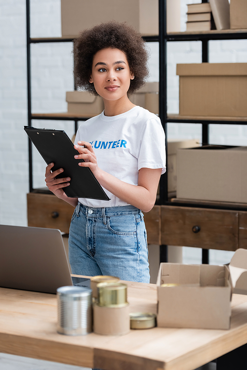 positive african american woman with clipboard looking away in volunteer center