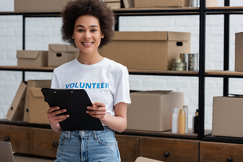 young african american volunteer with clipboard looking at camera in donation center