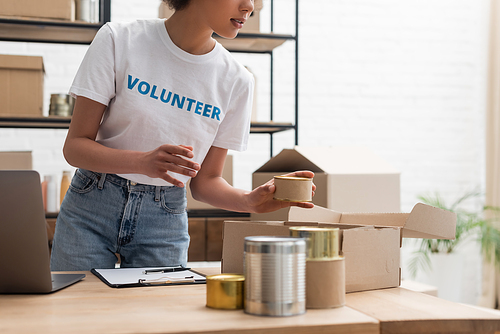 cropped view of african american woman sorting canned foodstuff in volunteer warehouse