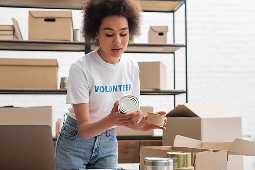 young african american woman sorting canned foodstuff in volunteer center