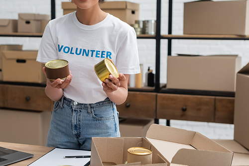 cropped view of african american woman holding canned foodstuff while working in donation warehouse