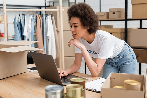 young african american woman working on laptop near canned food on blurred foreground