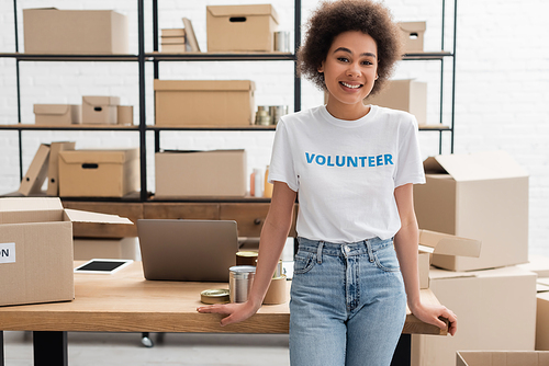 young african american volunteer smiling at camera near desk with gadgets in charity center