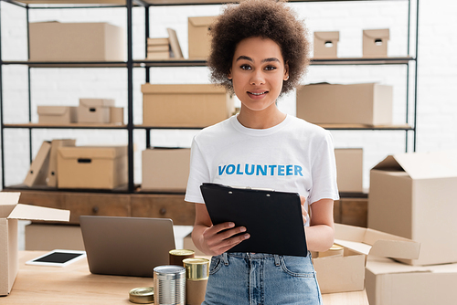 young african american woman with clipboard looking at camera in volunteer warehouse