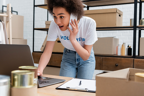 african american volunteer talking on cellphone near laptop in charity center