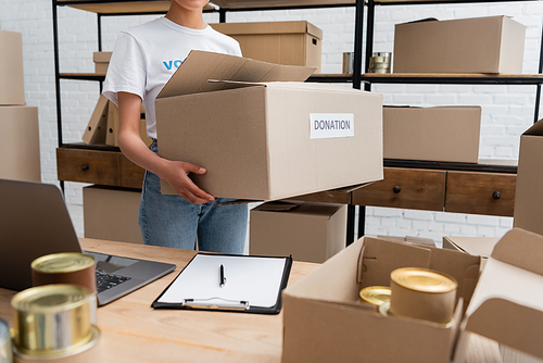 cropped view of african american woman holding donation box in charity warehouse