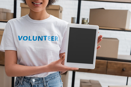 partial view of smiling african american volunteer holding digital tablet with blank screen in charity center