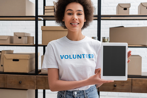 happy african american volunteer smiling at camera near digital tablet with blank screen