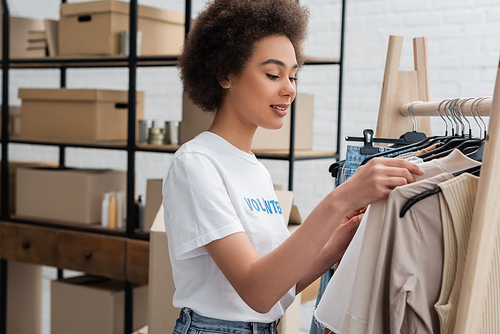 smiling african american volunteer sorting clothing in charity center