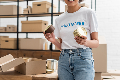 partial view of african american volunteer holding canned food in charity storehouse