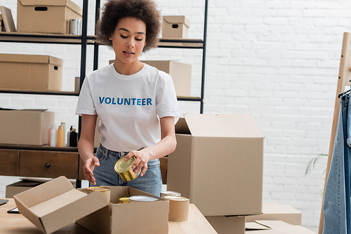 african american volunteer packing canned foodstuff in donation storehouse