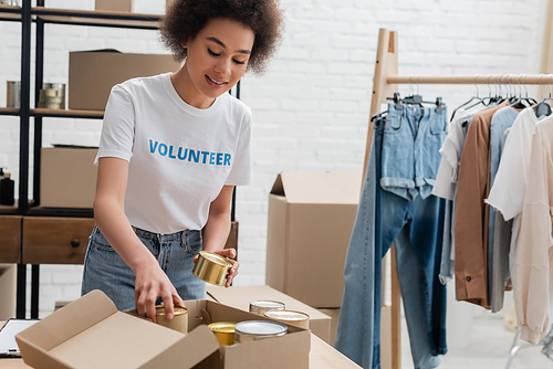 african american volunteer packing canned foodstuff in charity center