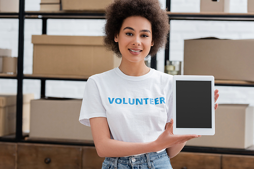 happy african american volunteer holding digital tablet with blank screen in charity center