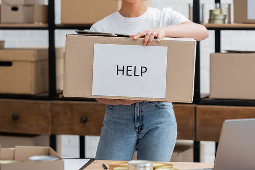 partial view of african american volunteer holding box with help lettering in charity center