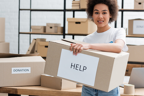 positive african american woman holding box with help lettering in volunteer center