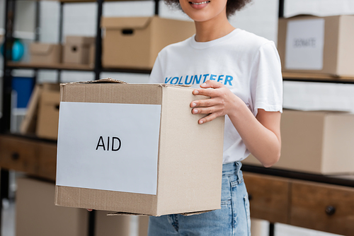 cropped view of african american volunteer holding box with aid lettering in charity warehouse