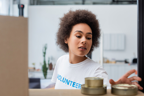 young african american volunteer near blurred tins in donation warehouse