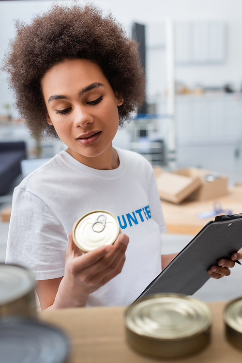 african american woman holding clipboard and canned food in charity center